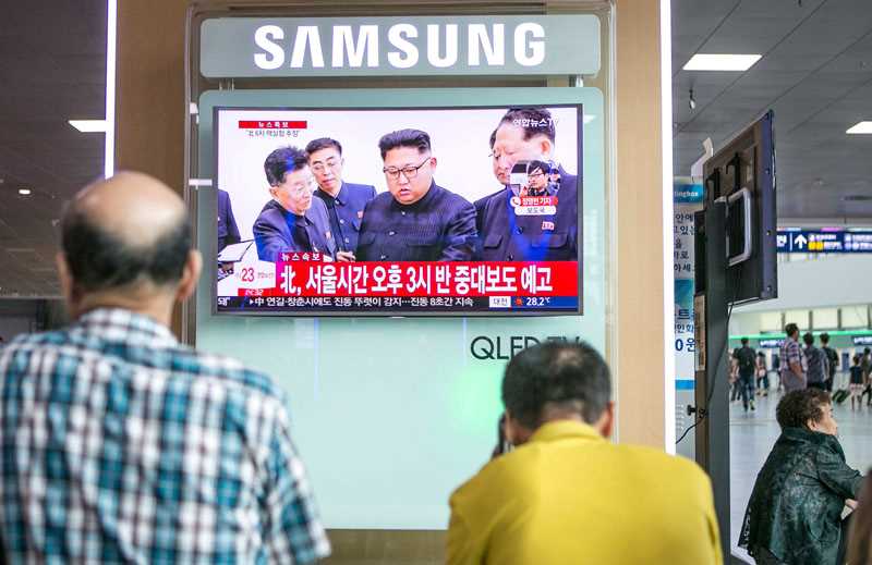 Två män i förgrunden tittar på en tv-skärm med nyheter om Nordkorea.