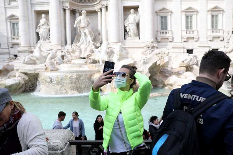 En kvinna med ansiktsmask tar en selfie framför Fontana di Trevi i Rom