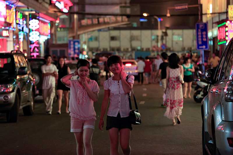 Två unga asiatiska kvinnor  iklädda shorts och sommarblusar promenerar på en gata.