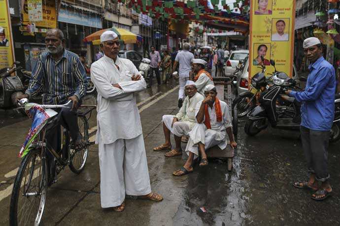 Foto med gatuscen i Mumbai. Till vänster en man på cykel och i mitten flera män som tittar in i kameran.