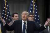 USA:s president Donald Trump med lyfta händer och blick i talarstolen, amerikanska flaggor i bakgrunden.