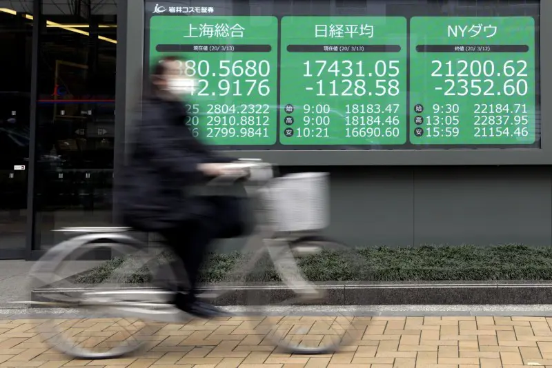 En kvinna med skyddsmask cyklar förbi en monitor med aktiekurser i Tokyo