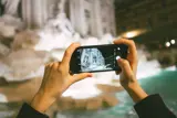 Foto: To hender som holder en mobil og fotograferer Fontana di Trevi i Roma.